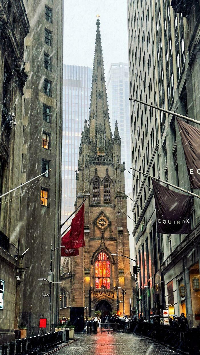 Gothic church facade in cityscape with snow falling, framed by tall buildings, highlighting fascinating architecture.