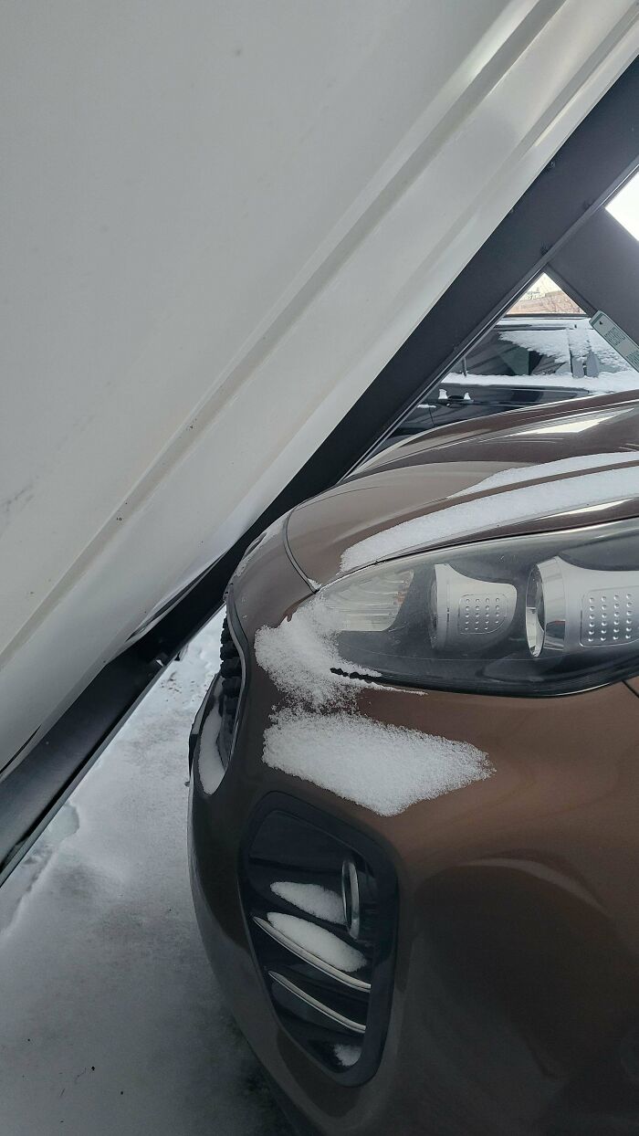 Close-up of a car partially covered in snow under a tilted white structure, showcasing a wild coincidence captured in a photo.