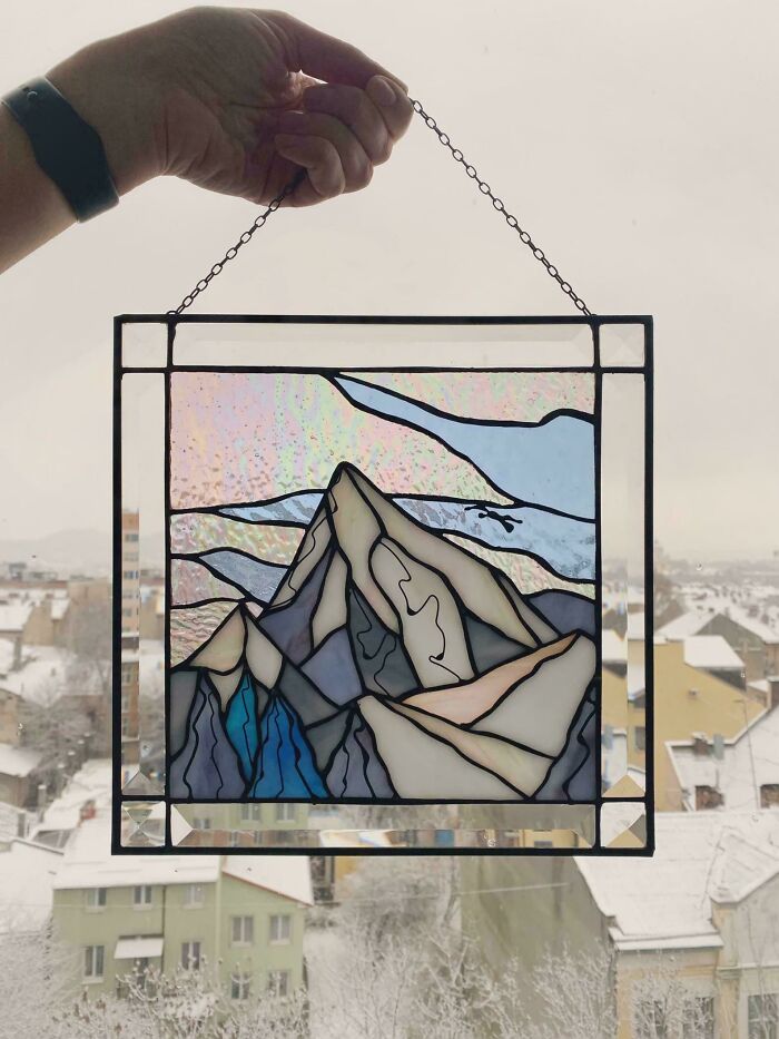 Stained glass DIY project featuring a mountain design, held against a snowy cityscape backdrop.