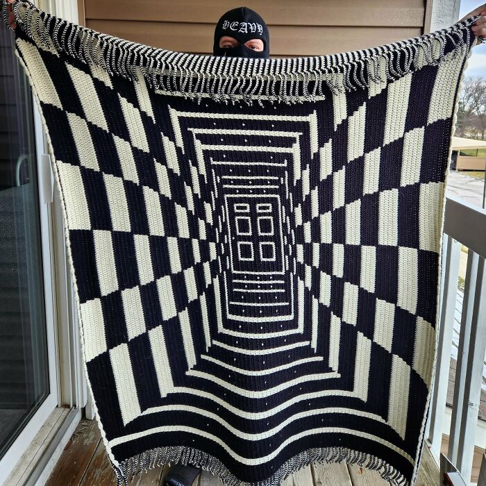 Person holding a black and white crochet blanket with an optical illusion pattern, showcasing proud crochet project skills.
