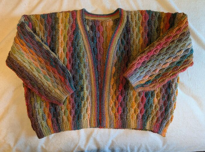 Multicolored crochet sweater with intricate cable patterns displayed on a light surface, showcasing crochet craftsmanship.