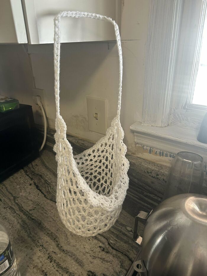 White crochet hanging bag with mesh pattern displayed on kitchen counter, showcasing proud crochet project by enthusiast.
