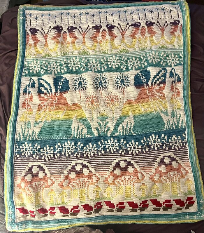 Crochet blanket featuring butterflies, flowers, and mushrooms in vibrant colors displayed on a dark background.