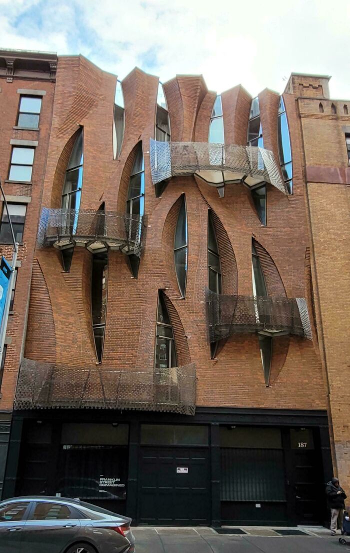 Unique architectural feats with curved brickwork and metal balconies on an urban building facade in a city setting.