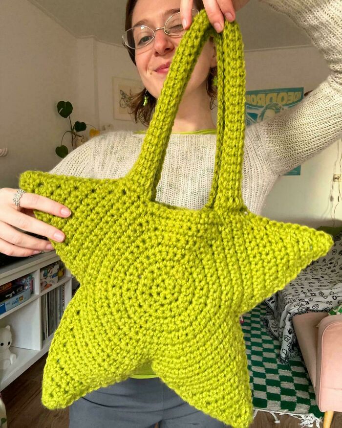 Woman proudly holding a bright green star-shaped crochet bag, showcasing her creative crochet project at home.