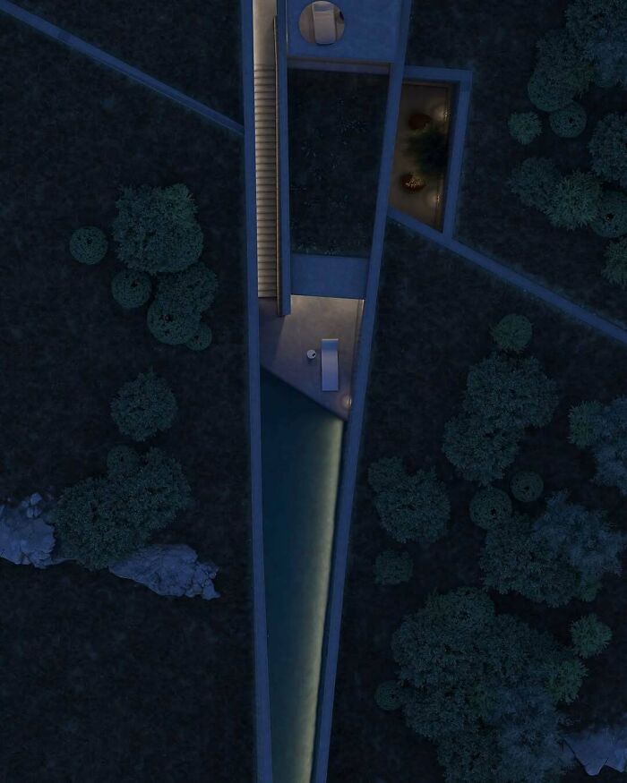 Aerial view of an interesting V-shaped building with glowing lights set in dense foliage at night.