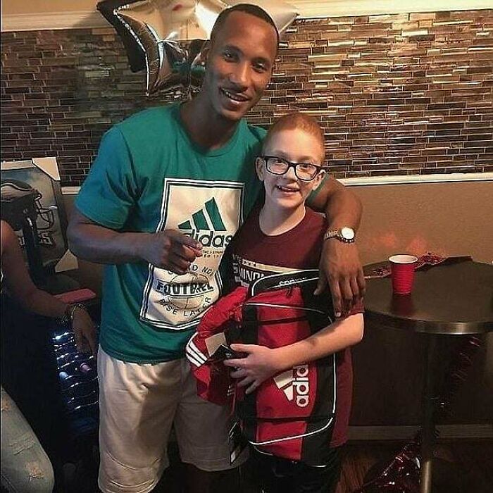 Two people smiling together indoors, one wearing an Adidas shirt, holding Adidas items. Fascinating moment captured.