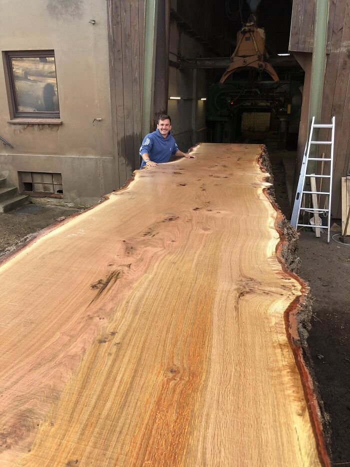 Man standing beside an enormous wooden slab, showcasing fascinating craftsmanship.