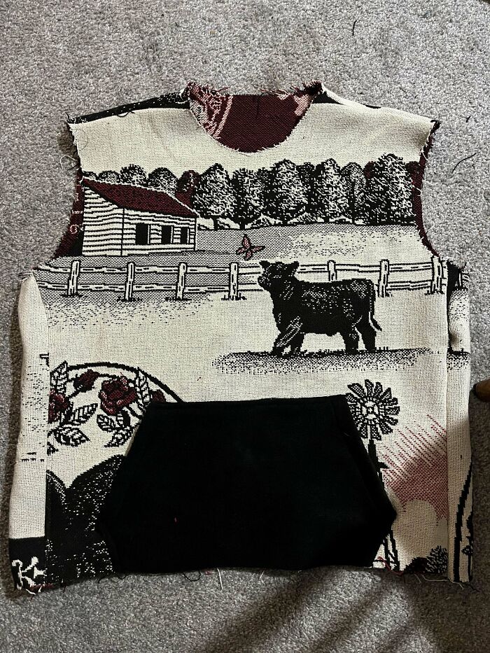 DIY project tapestry sweater with a farm scene featuring a cow and barn, laid flat on a gray surface.
