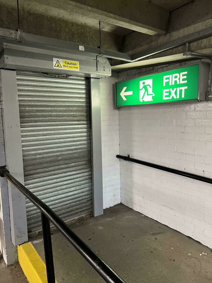 Blocked fire exit behind closed metal shutter with caution sign above, showing employees ignoring safety protocol risks.