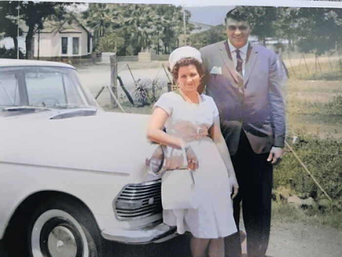A vintage couple poses by a classic car, capturing a moment from history.