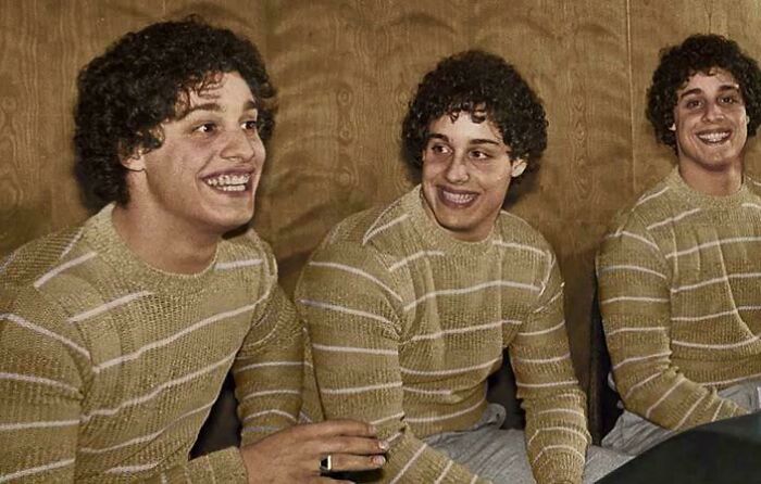 Three men in identical striped sweaters sit together, smiling, showcasing fascinating resemblance.
