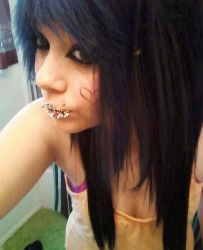 Young person with dark emo hairstyle, creative makeup, and facial piercings, showcasing a unique style during their blunder years.