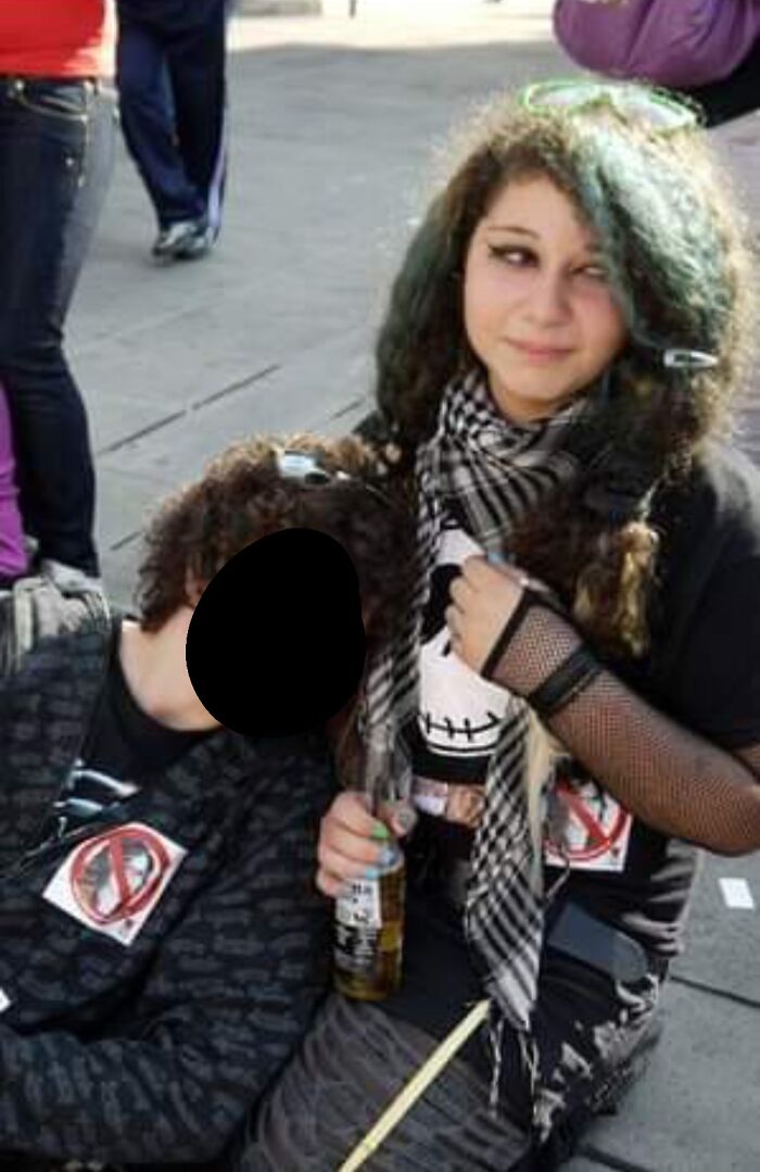 Teen in alternative style outfit with a scarf and mesh sleeves, holding a drink, embodying blunder years fashion.