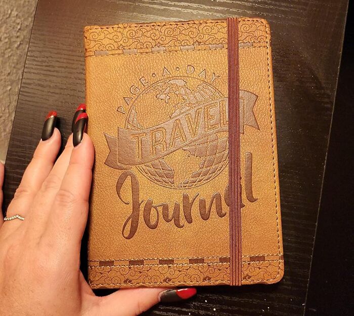 Travel journal on a table with a hand, ready to document a year of adventures.