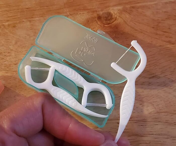Travel essentials include floss picks in a portable case on a wooden surface.