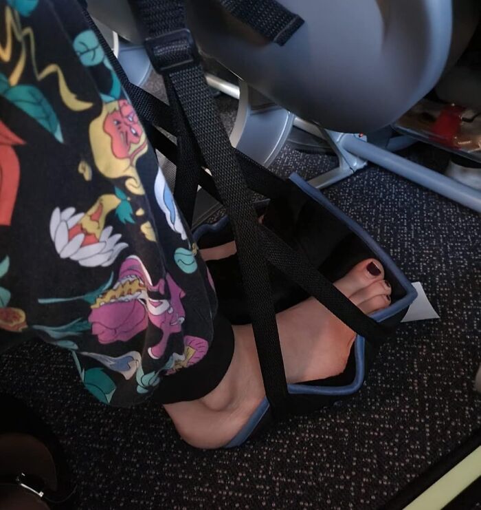 Feet in a travel footrest on an airplane, wearing colorful leggings.