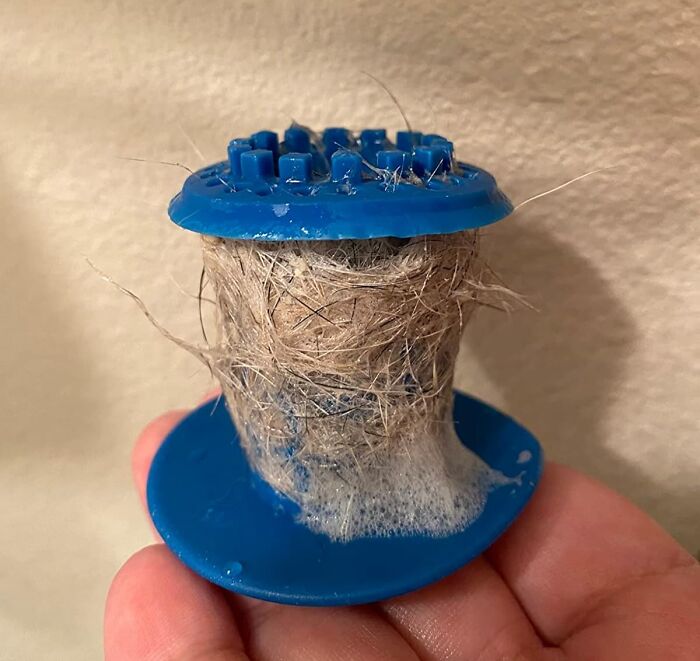 Blue hair catcher filled with hair in a hand, showcasing a simple hack for easy drain cleaning.