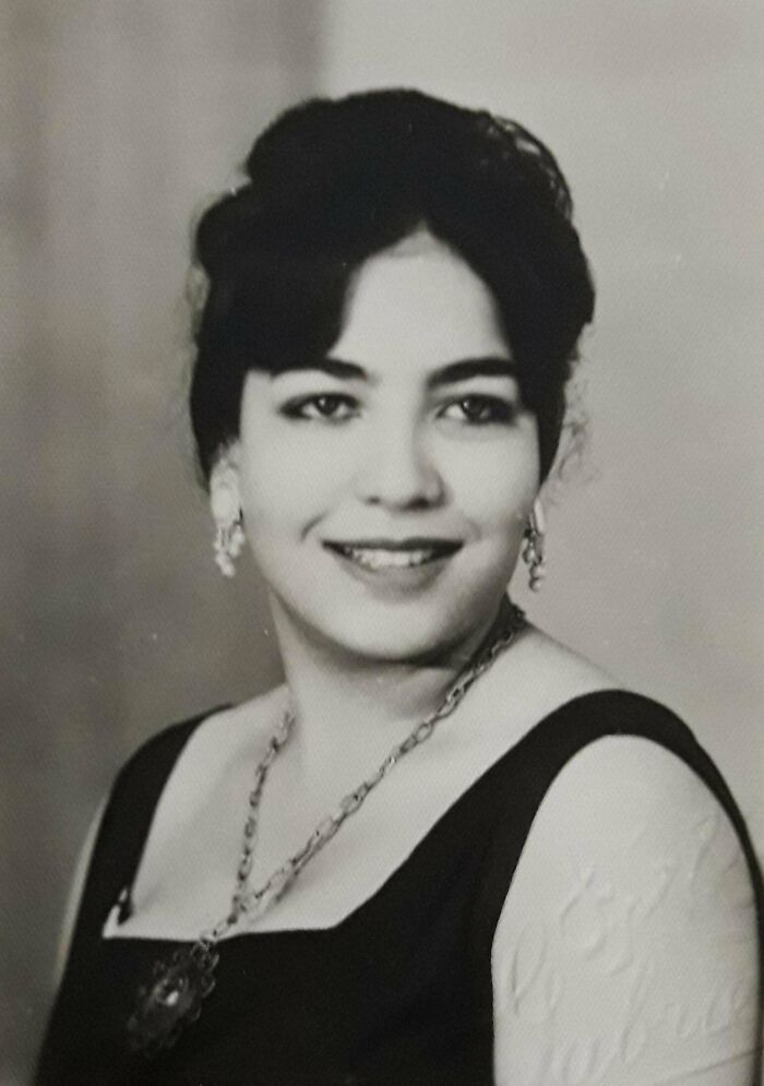 Historic portrait of a woman in a dark dress, wearing earrings and a necklace, smiling gently.