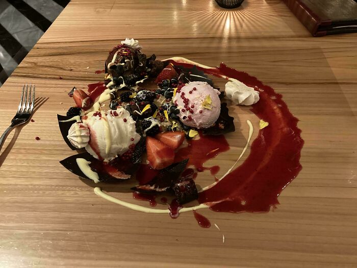 A dessert with ice cream and fruit served directly on a wooden table, showcasing ridiculous food presentation in restaurants.