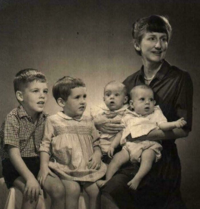 A vintage family portrait with a woman holding two babies, and two children sitting beside her.