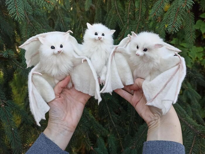 Hands holding three adorable white bats against a backdrop of greenery, showcasing fascinating animal facts.