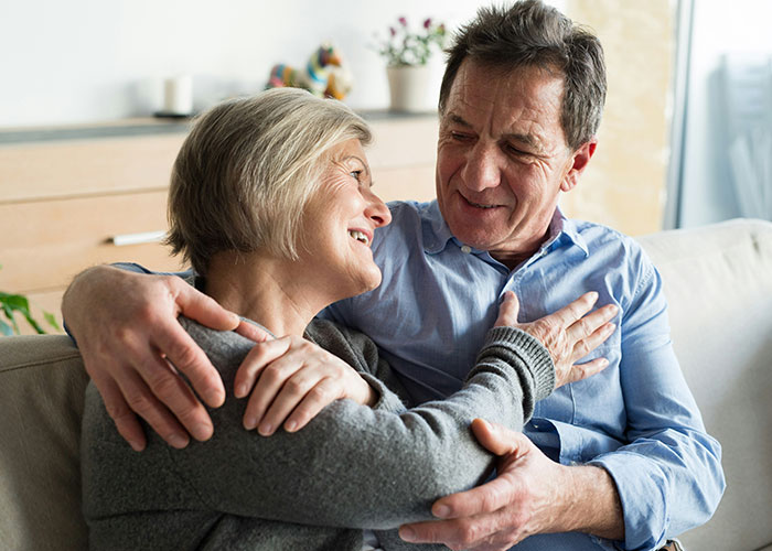 A happy couple sitting on a couch, embracing and smiling, discussing financial income combination. A happy couple sitting on a couch, embracing and smiling, discussing financial income combination.