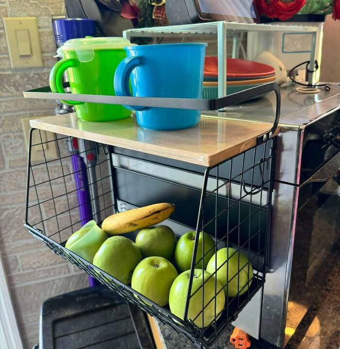 Wire basket holding green apples and a banana, with colorful plastic mugs on top, reorganizing your fridge and pantry space.