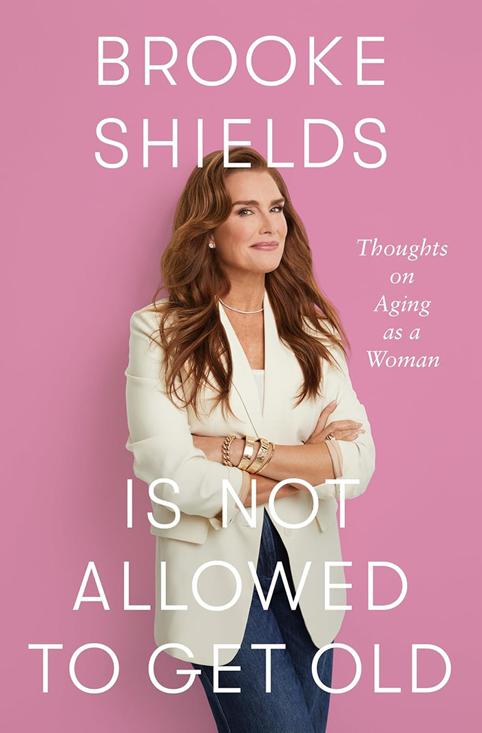 Brooke Shields in a white blazer, posing against a pink background, discussing aging and personal revelations. Brooke Shields in a white blazer, posing against a pink background, discussing aging and personal revelations.
