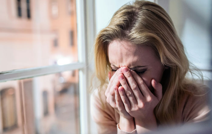 A distressed woman crying by a window, representing guilt and emotional struggle over adoption decision. A distressed woman crying by a window, representing guilt and emotional struggle over adoption decision.