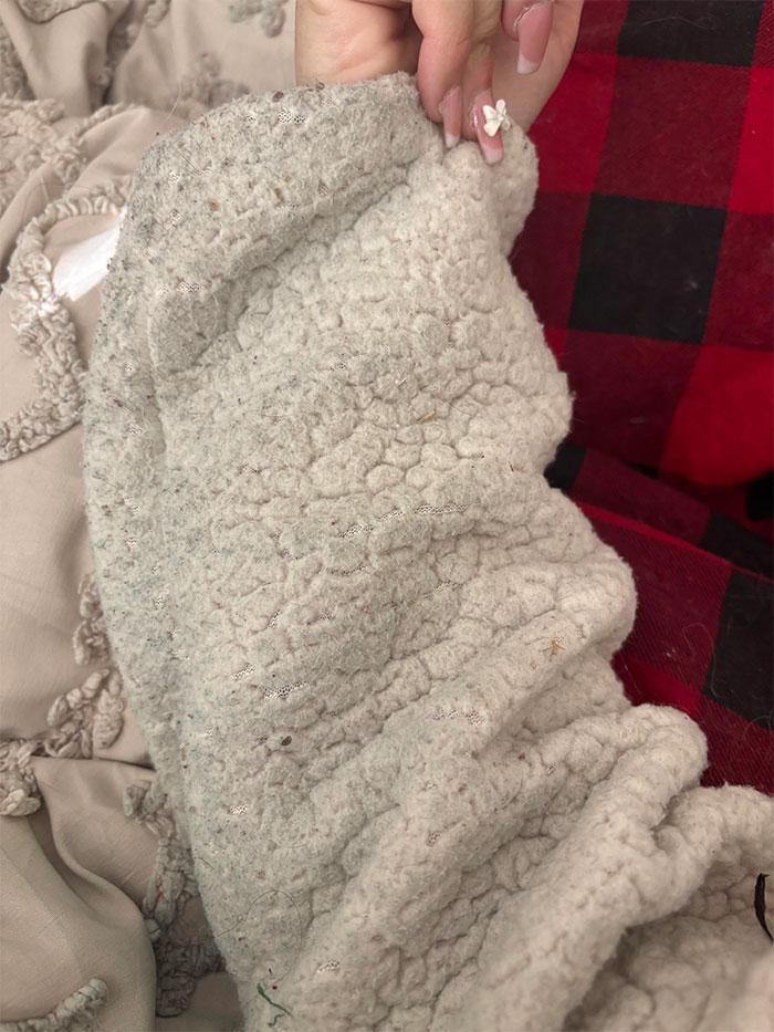 Close-up of a textured white blanket with a woman's hand holding it, suggesting recent stains in a home setting. Close-up of a textured white blanket with a woman's hand holding it, suggesting recent stains in a home setting.