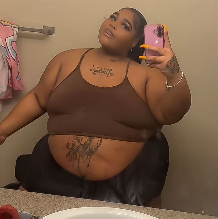 Plus size woman taking a selfie in the mirror, wearing a brown top with tattoos visible. Plus size woman taking a selfie in the mirror, wearing a brown top with tattoos visible.