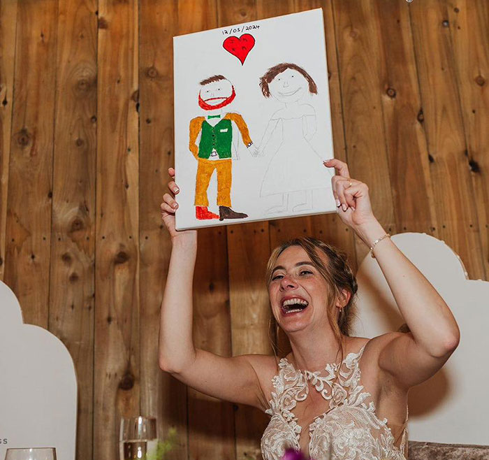 Woman joyfully holding a viral painting of herself and husband, featuring simple drawings with a heart above. Woman joyfully holding a viral painting of herself and husband, featuring simple drawings with a heart above.