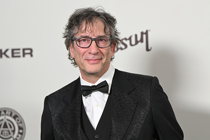 Neil Gaiman in a formal suit poses at an event. Neil Gaiman in a formal suit poses at an event.