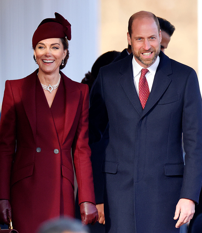 Prince William smiling in a suit beside Kate Middleton in a burgundy coat and hat on a sunny day. Prince William smiling in a suit beside Kate Middleton in a burgundy coat and hat on a sunny day.
