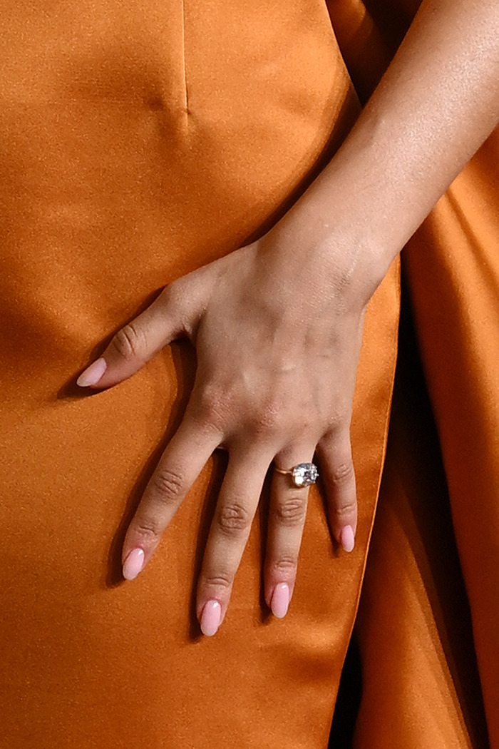 Engagement ring on Zendaya's hand over orange dress. Engagement ring on Zendaya's hand over orange dress.