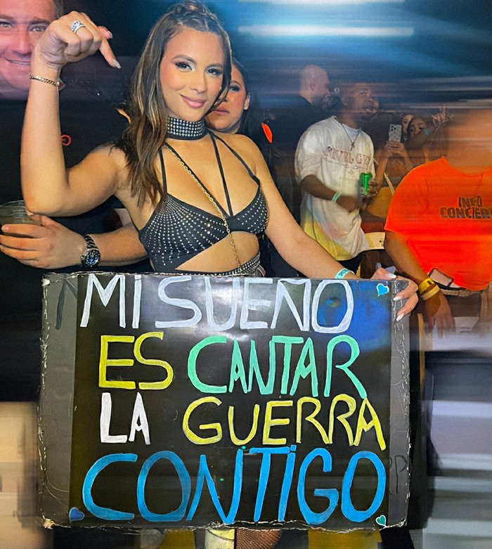 Influencer at concert holding a sign, surrounded by a lively crowd, with colorful lights and energy. Influencer at concert holding a sign, surrounded by a lively crowd, with colorful lights and energy.