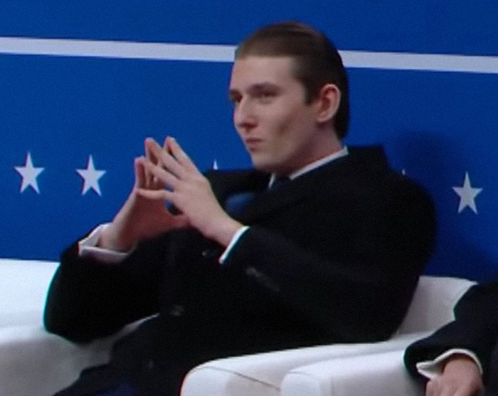 Barron Trump in a suit making a significant hand gesture during an inaugural event. Barron Trump in a suit making a significant hand gesture during an inaugural event.