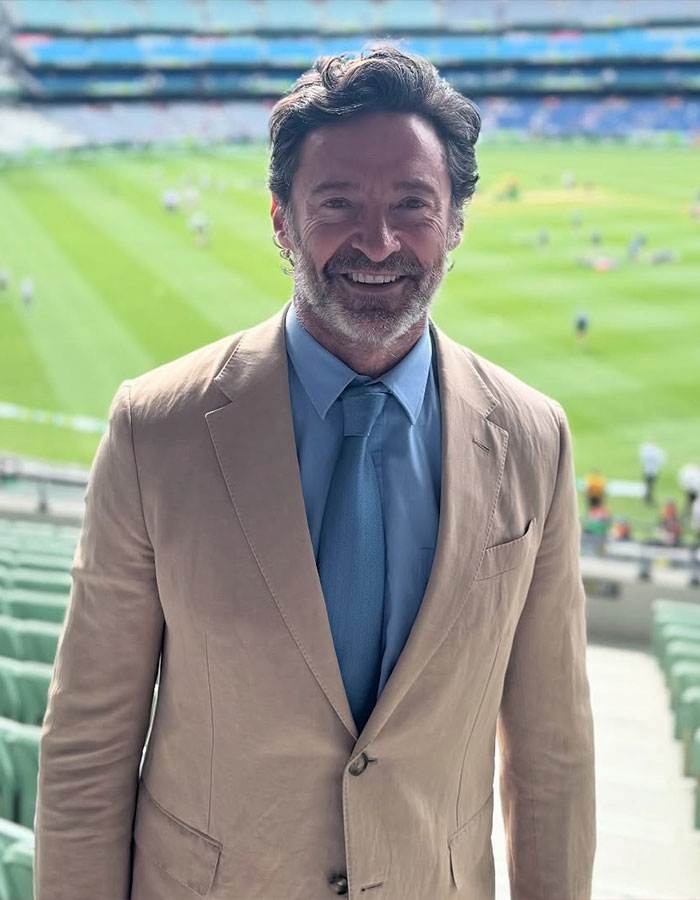 Man in a beige suit with a blue tie at the Australian Open, smiling against a background of a sports field. Man in a beige suit with a blue tie at the Australian Open, smiling against a background of a sports field.