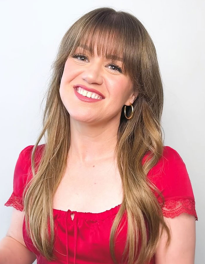 Person in a red top smiling, with long hair and hoop earrings, related to Hollywood beauty trends. Person in a red top smiling, with long hair and hoop earrings, related to Hollywood beauty trends.