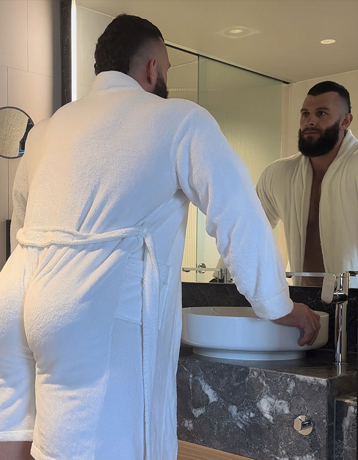 Man in a white robe looks at his reflection in a bathroom mirror, related to male stripper experiences at bachelorette parties. Man in a white robe looks at his reflection in a bathroom mirror, related to male stripper experiences at bachelorette parties.