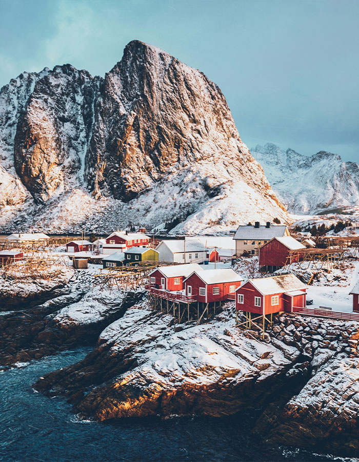 Snowy Norwegian village with colorful houses and dramatic cliffs, illustrating a secret to never feeling cold. Snowy Norwegian village with colorful houses and dramatic cliffs, illustrating a secret to never feeling cold.