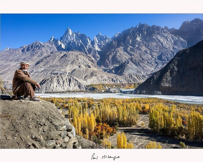 Mountain landscape with a person sitting on a rocky edge, captured by Paul McKenzie.