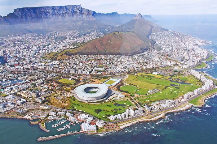 Aerial view of coastal city with stadium, mountain, and green areas showcasing urban landscape. Aerial view of coastal city with stadium, mountain, and green areas showcasing urban landscape.