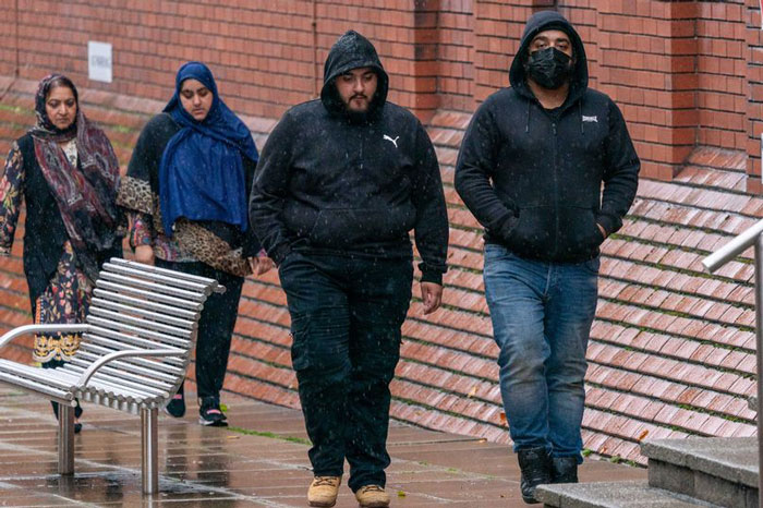 People walking outside a brick building in rainy weather, wearing hooded jackets. People walking outside a brick building in rainy weather, wearing hooded jackets.