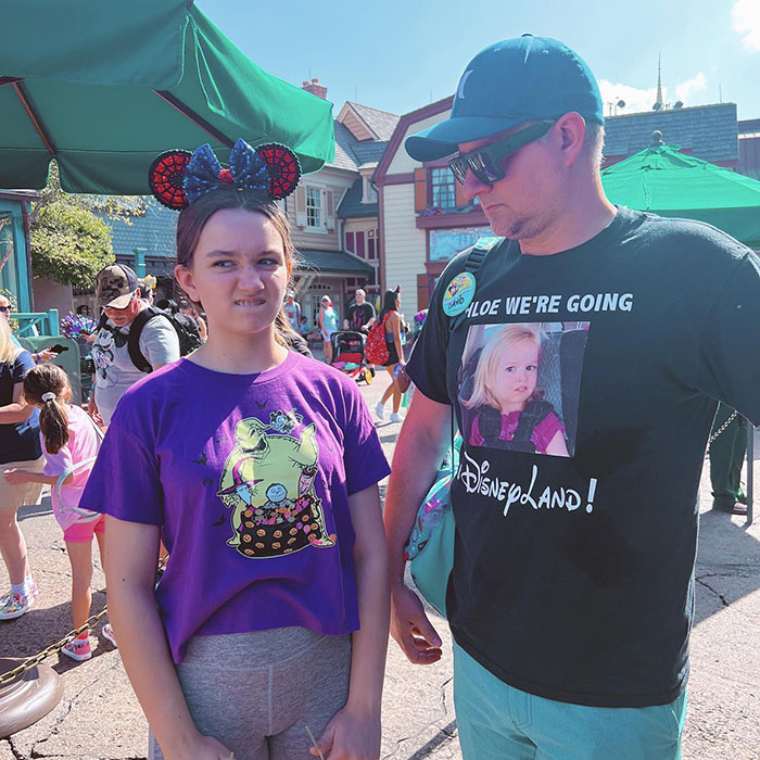 Girl from the viral meme making a funny face at a theme park, accompanied by a man in a shirt referencing the meme. Girl from the viral meme making a funny face at a theme park, accompanied by a man in a shirt referencing the meme.