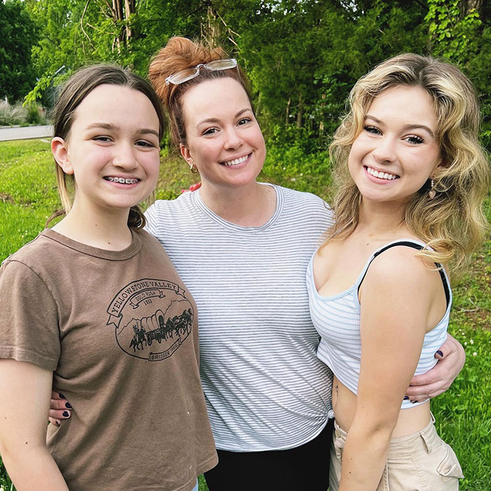 Mother and two daughters smiling outdoors, related to 'Side-Eyeing Chloe' meme. Mother and two daughters smiling outdoors, related to 'Side-Eyeing Chloe' meme.