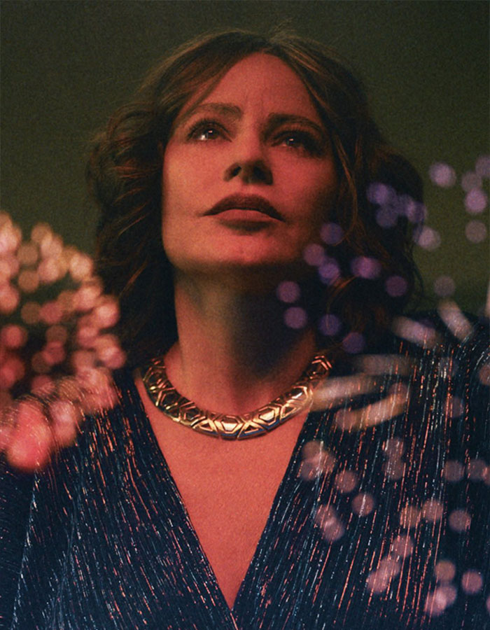 I'm not sure who this is, but here's an alt text for the image: "Woman with a stylish necklace gazing upwards amidst abstract light patterns. I'm not sure who this is, but here's an alt text for the image: "Woman with a stylish necklace gazing upwards amidst abstract light patterns.