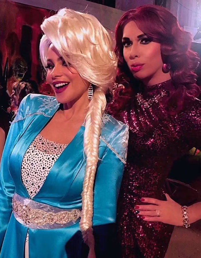 Two individuals in glamorous costumes at an event, with one wearing a blue dress and elaborate wig. Two individuals in glamorous costumes at an event, with one wearing a blue dress and elaborate wig.
