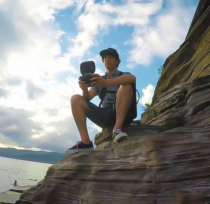 Man sitting on a rocky cliff, holding a camera against a scenic backdrop, reminiscent of MySpace founder. Man sitting on a rocky cliff, holding a camera against a scenic backdrop, reminiscent of MySpace founder.